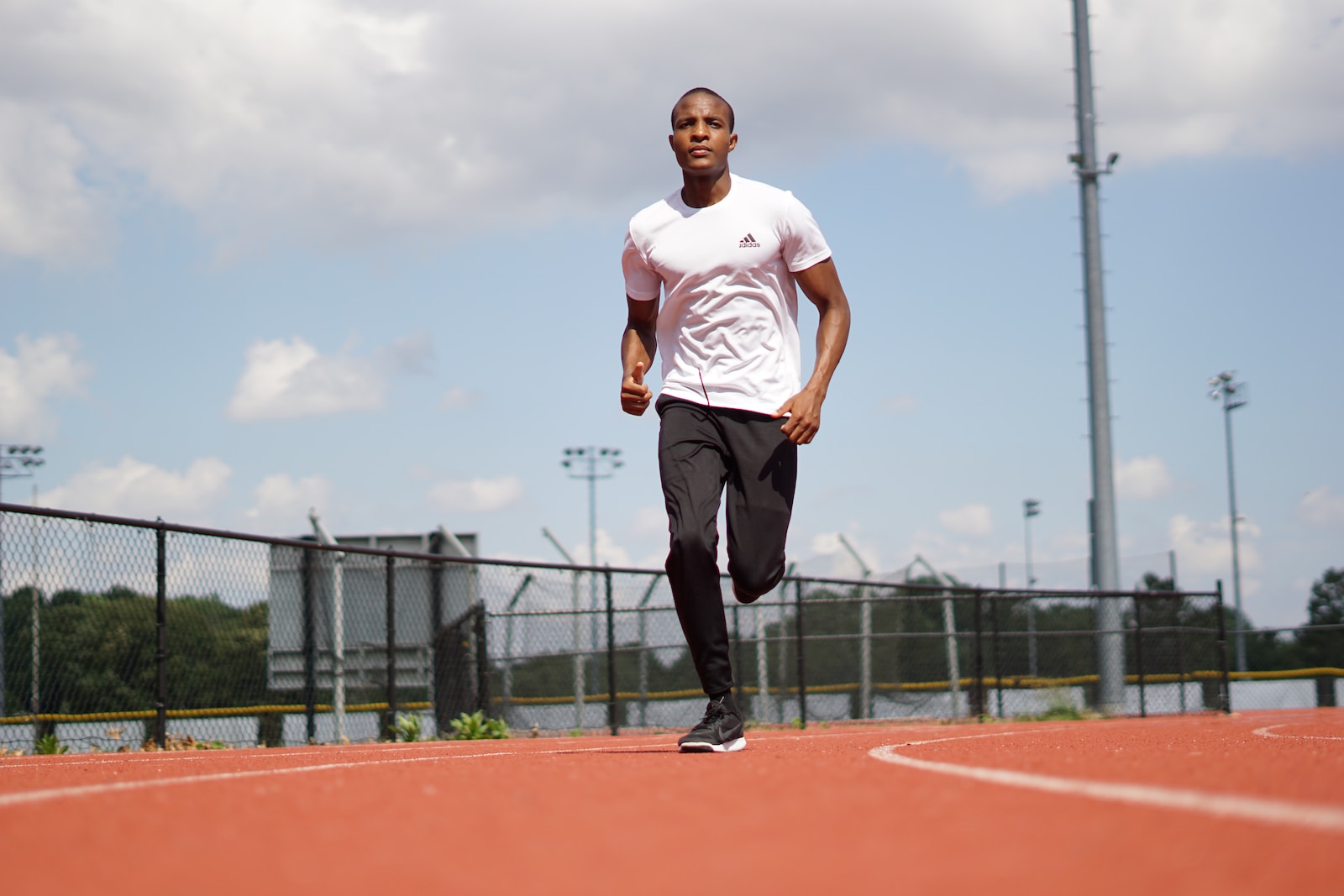 man in white crew neck t-shirt and black pants standing on track field during daytime
